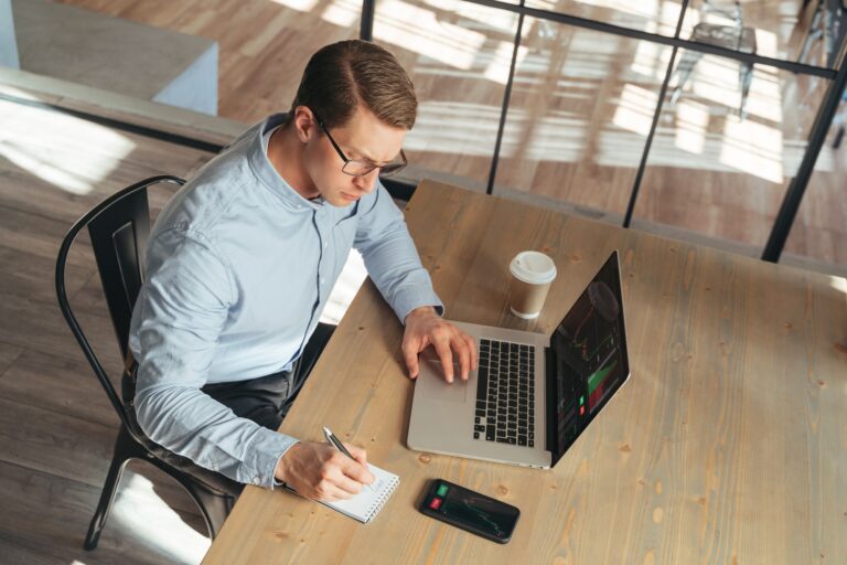 Top view of crypto trader working online, noting down info after checking price prediction chart