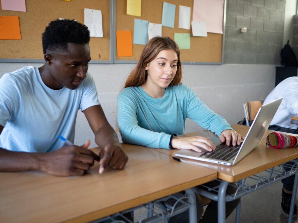 Two multiethnic students work as a team in class with a laptop