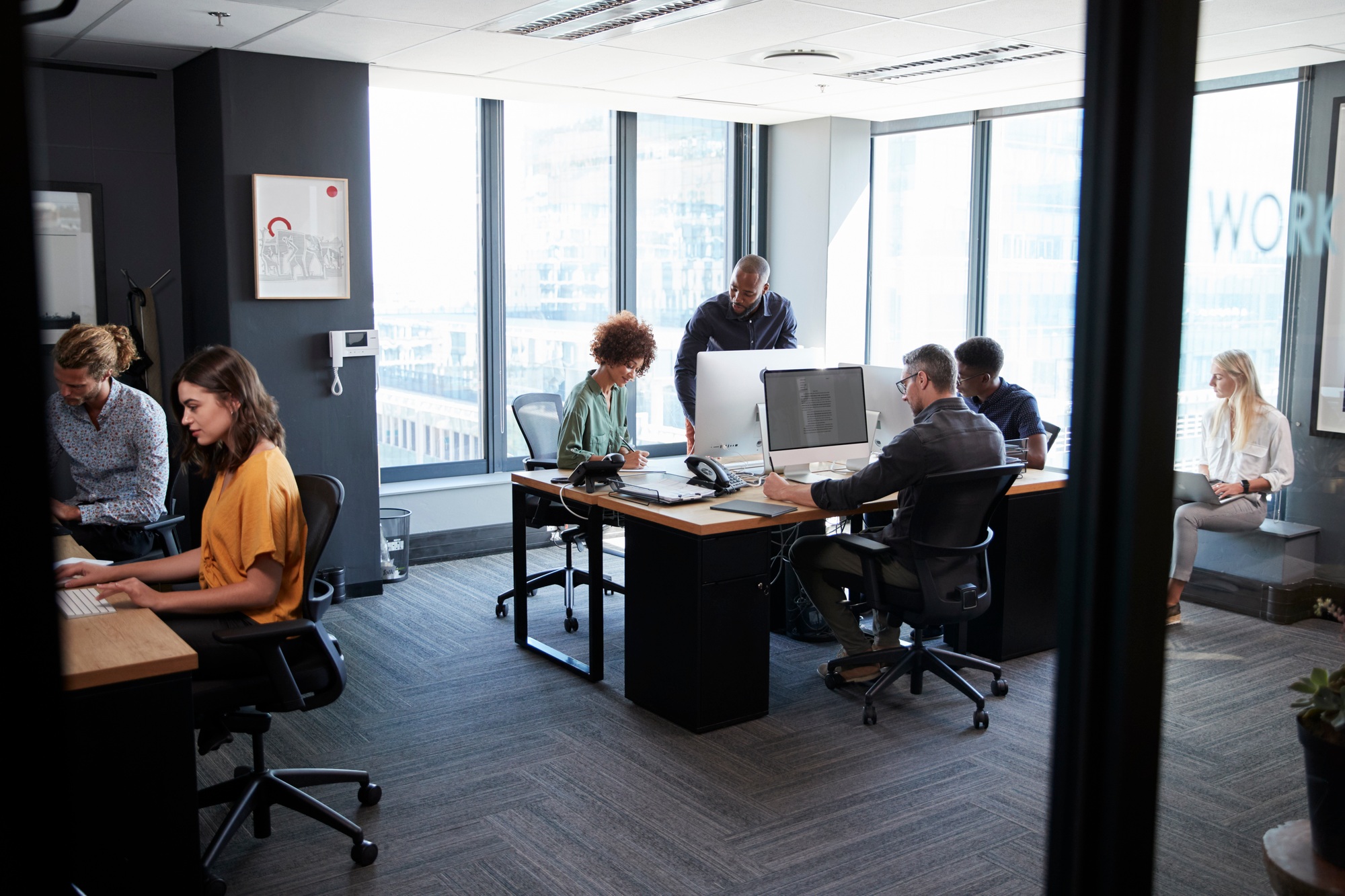 Young creative team working together at computers in a casual office, seen from doorway