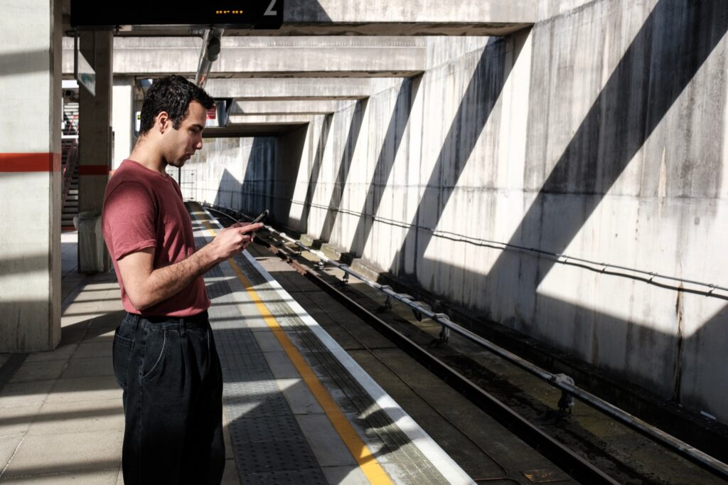 Young male waiting for a train and using mobile phone.