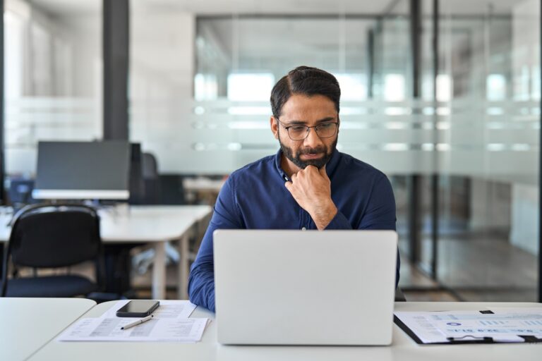 Busy Indian business man thinking on data management working on laptop.