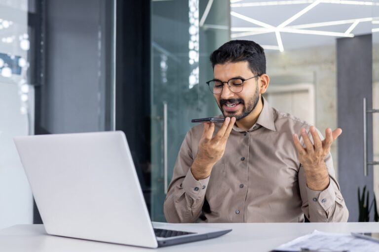 Professional man using voice assistant on smartphone at desk