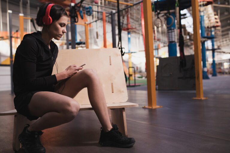 Woman with headphones and device sitting in gym