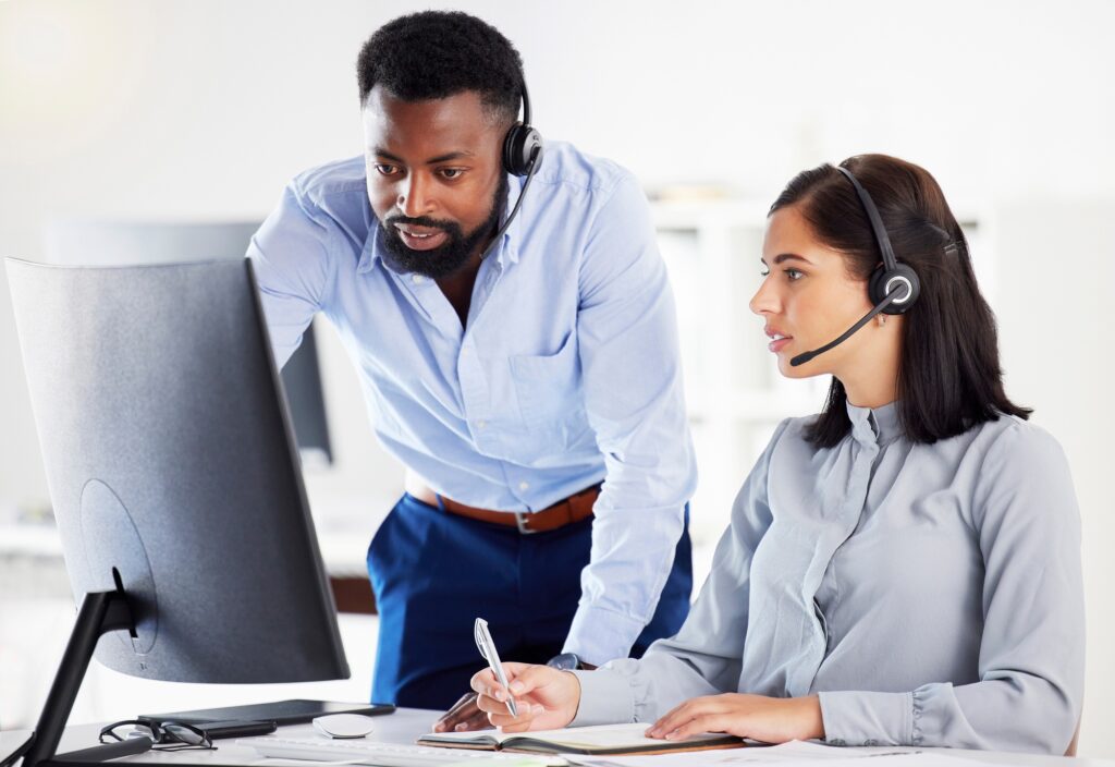 Young african american call centre telemarketing agent training new caucasian assistant on a comput