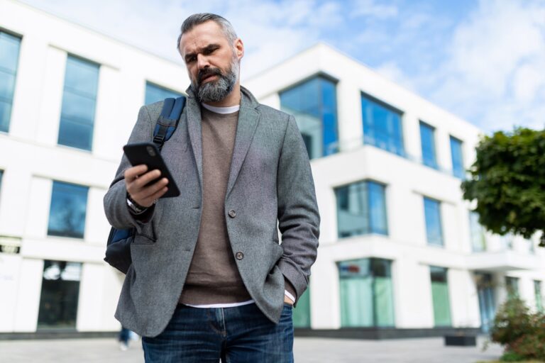 adult male software engineer leaves the office and looks at the mobile phone