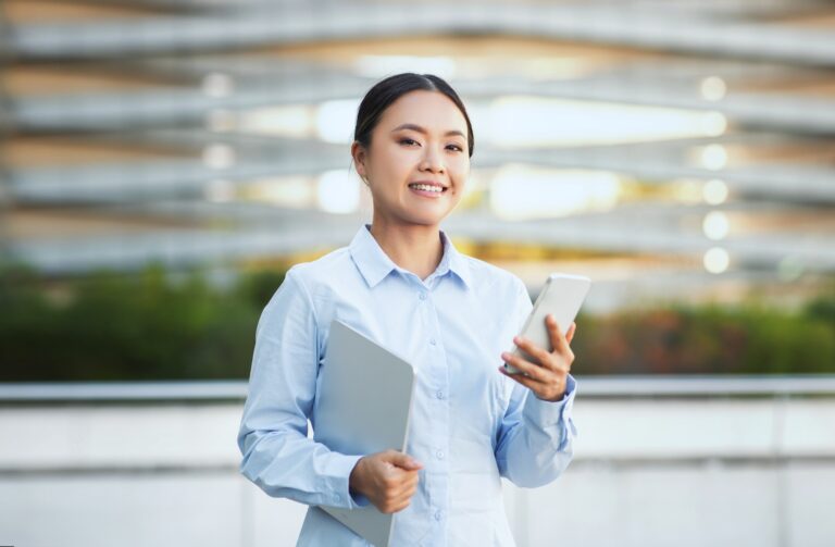 Asian Businesswoman Holding Smartphone and Smiling Outdoors