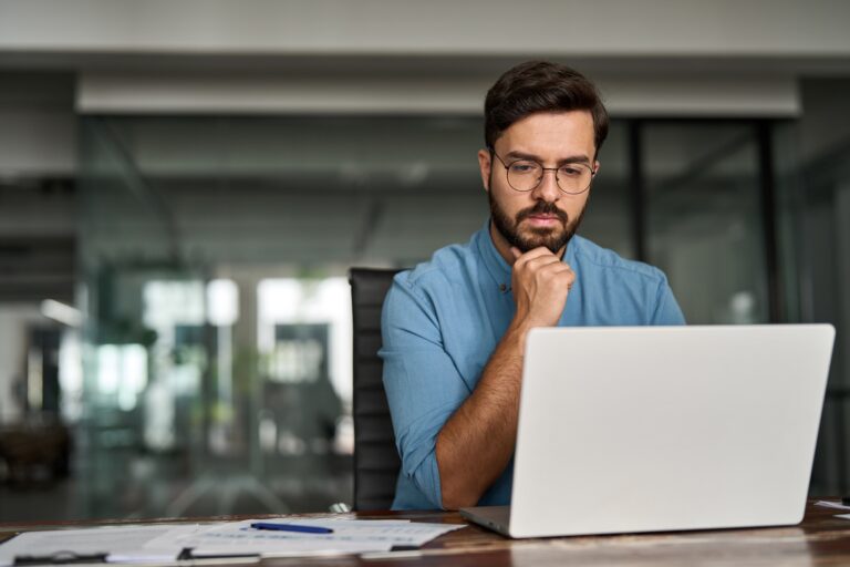 Busy young business man thinking on online investment working on laptop.