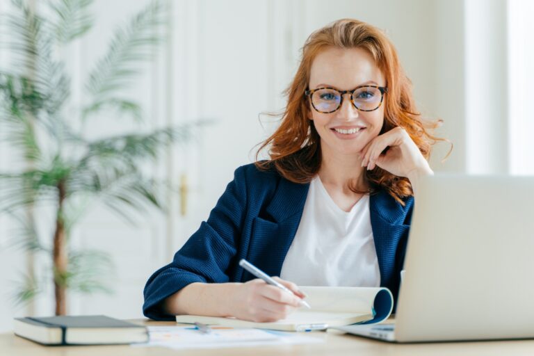 Happy successful female writes checklist in notepad, works on creative ideas for project