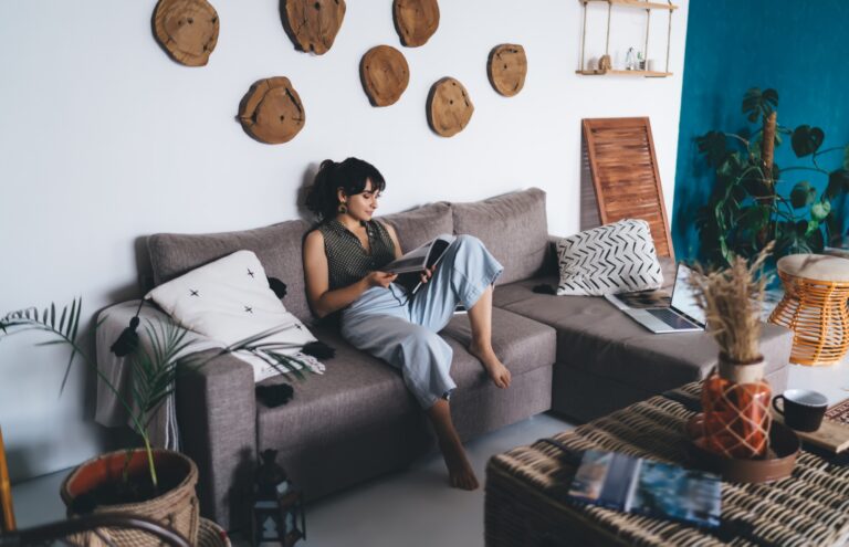 Young barefoot female reading journal in living room