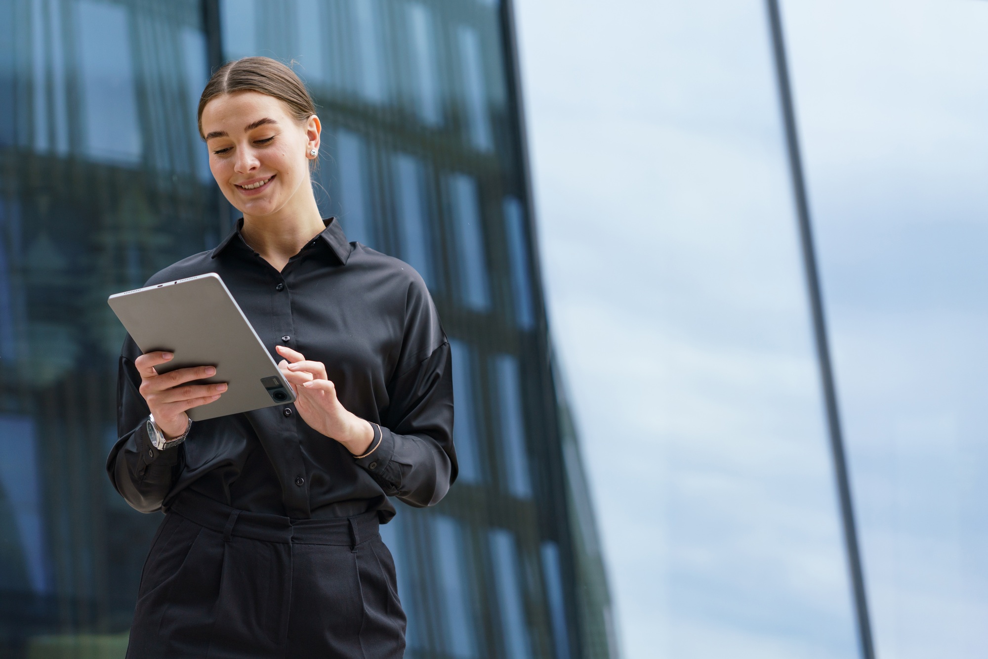 smiling businesswoman in black, interacting with a tablet, reflects modern professionalism and tech