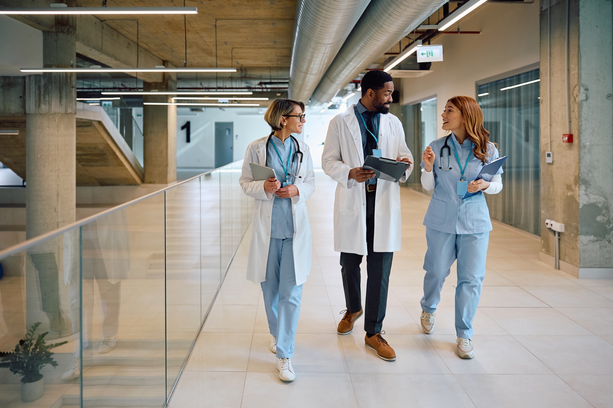 happy black doctor and his female colleagues communicating while walking through hospital hallway.