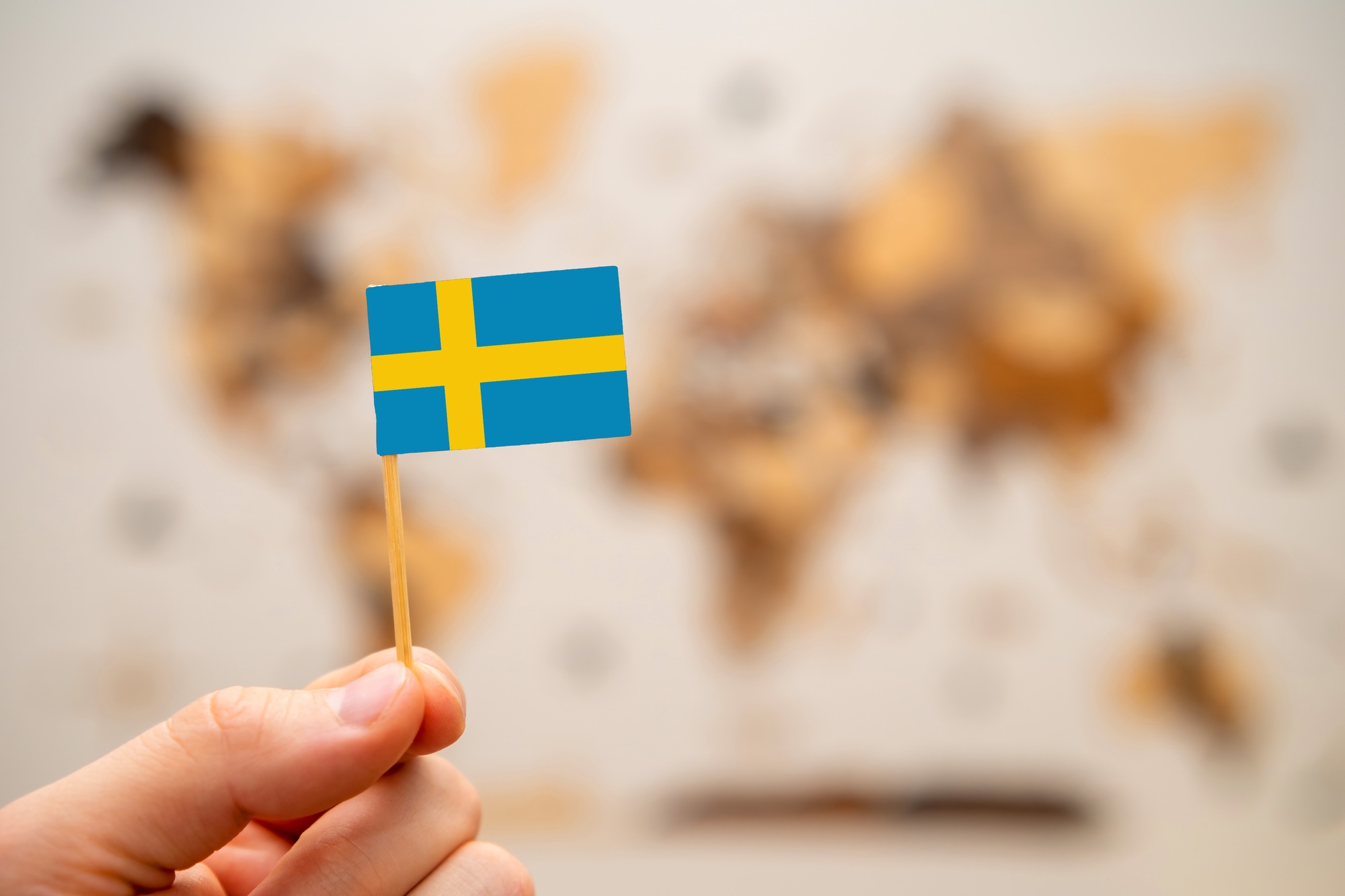 sweden flag in mans hand on the world map background.
