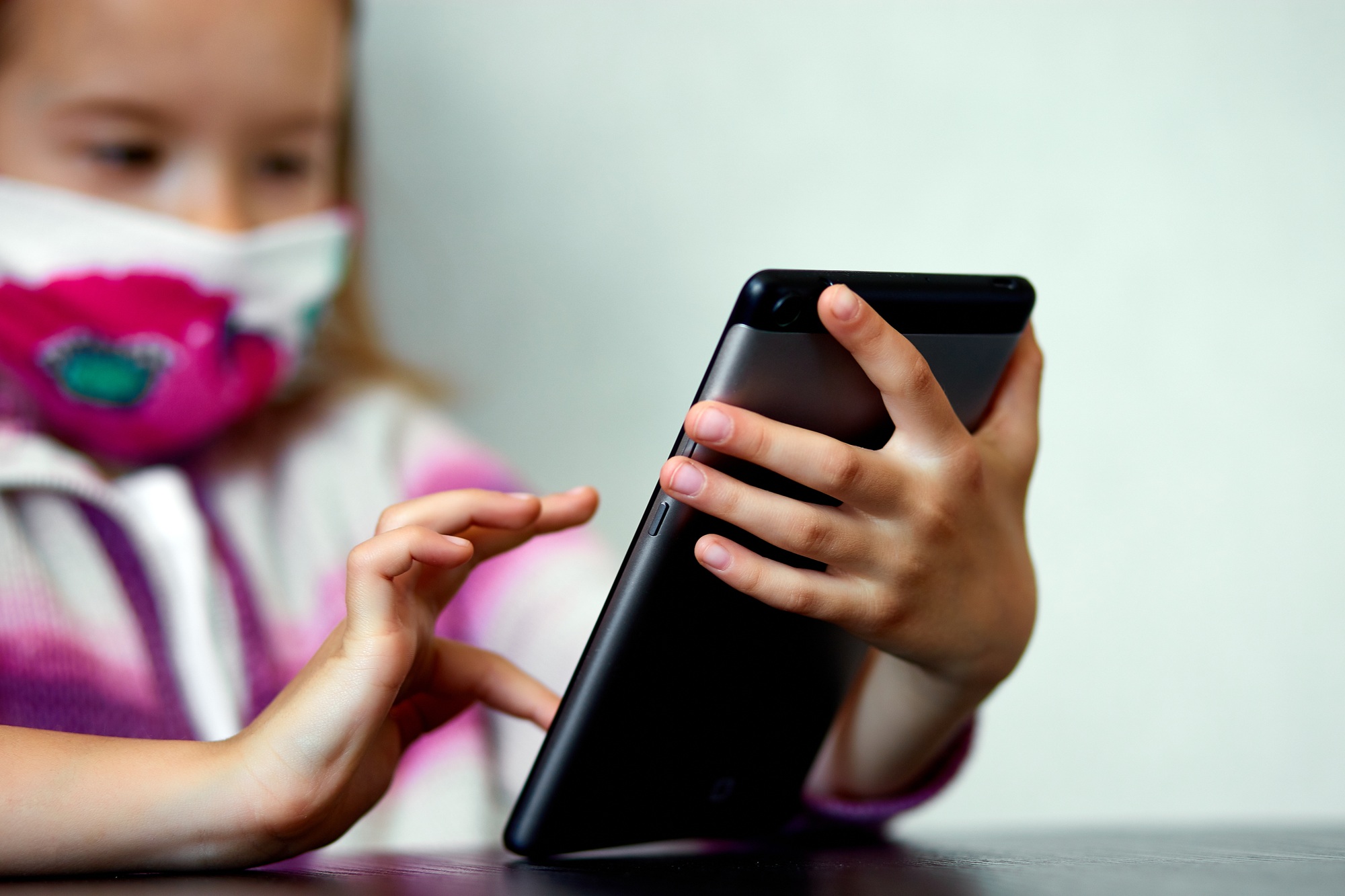 Meta Under Fire: How New AI Chatbots Were Allowed to Flirt with Children young child girl at home, wearing a protection mask and gaming on a tablet, coronavirus quarantine.