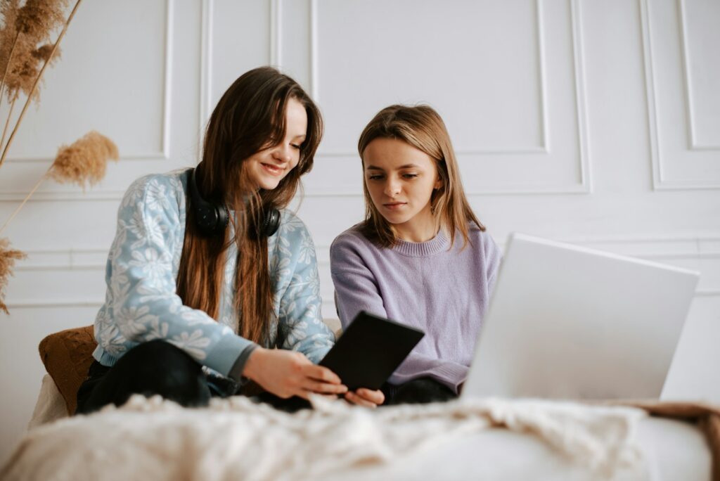 two girls sitting on a bed looking at a laptop