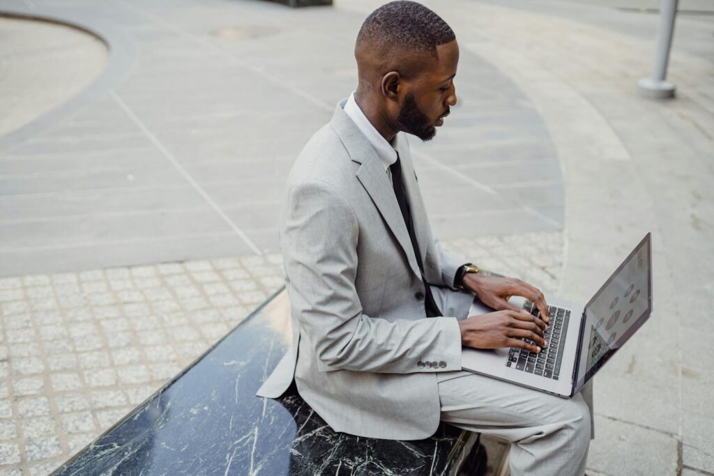 Business professional in a suit working on a laptop outdoors in an urban location.