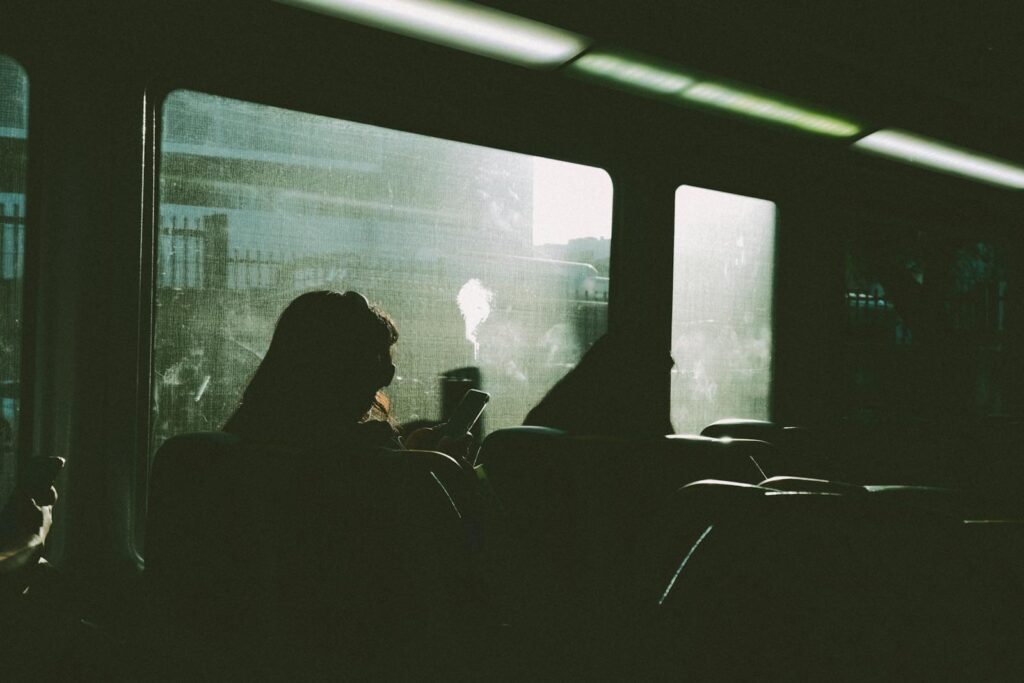 Silhouette of a person using a phone on a train journey, sunlight streaming in.