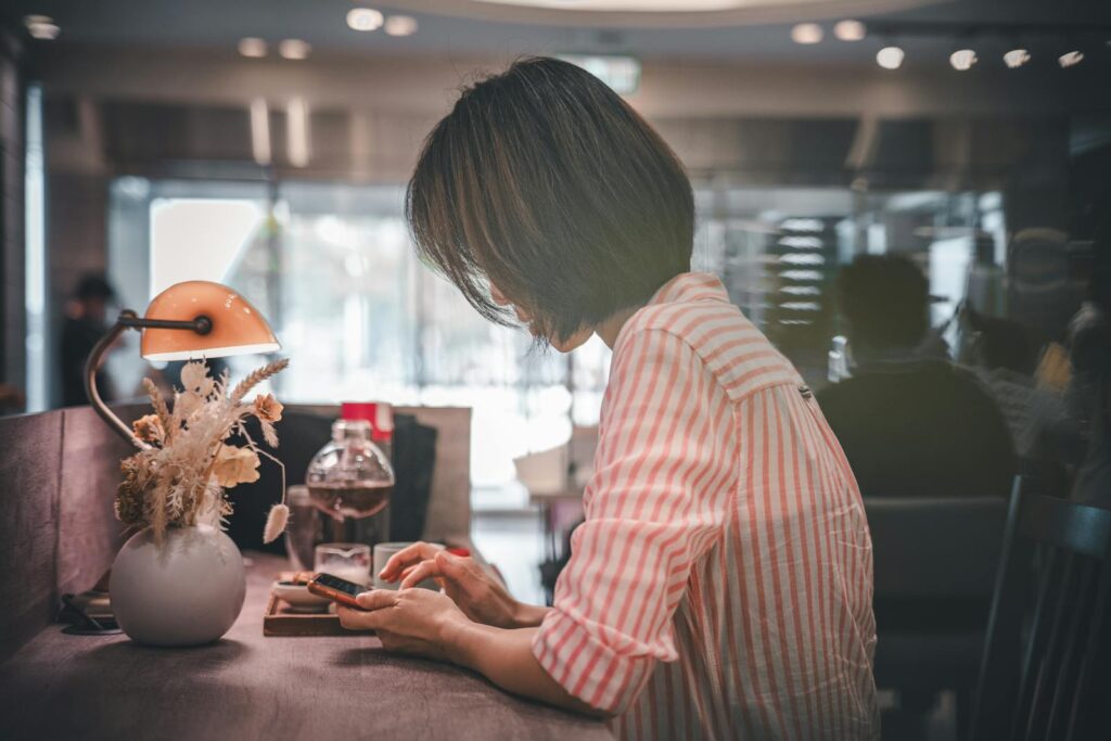 A woman in a café using a smartphone, surrounded by warm lighting and a cozy atmosphere.