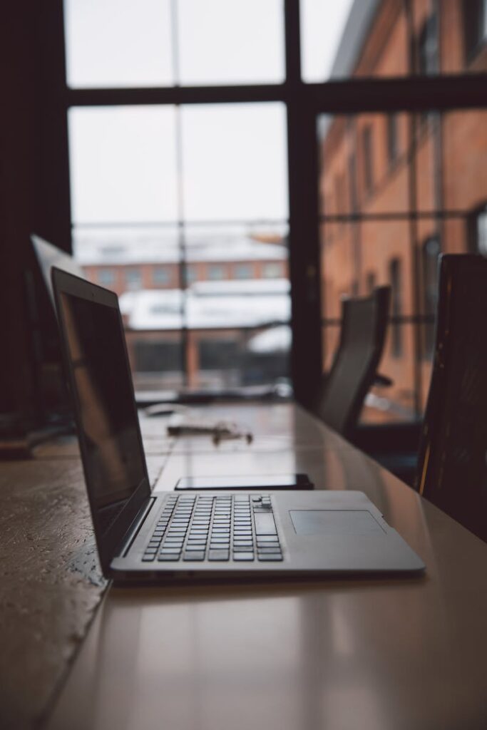 Open laptop on a wooden desk in a contemporary office space with large windows.
