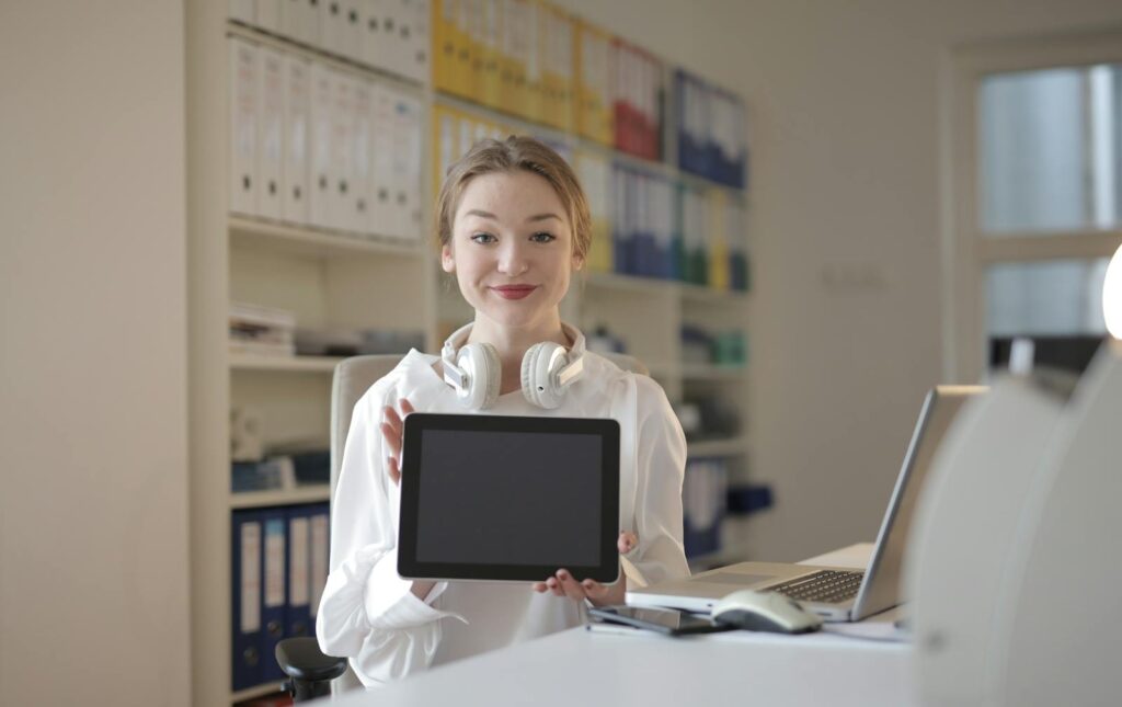 Smiling woman in office holding a tablet, exemplifying digital lifestyle and remote work.