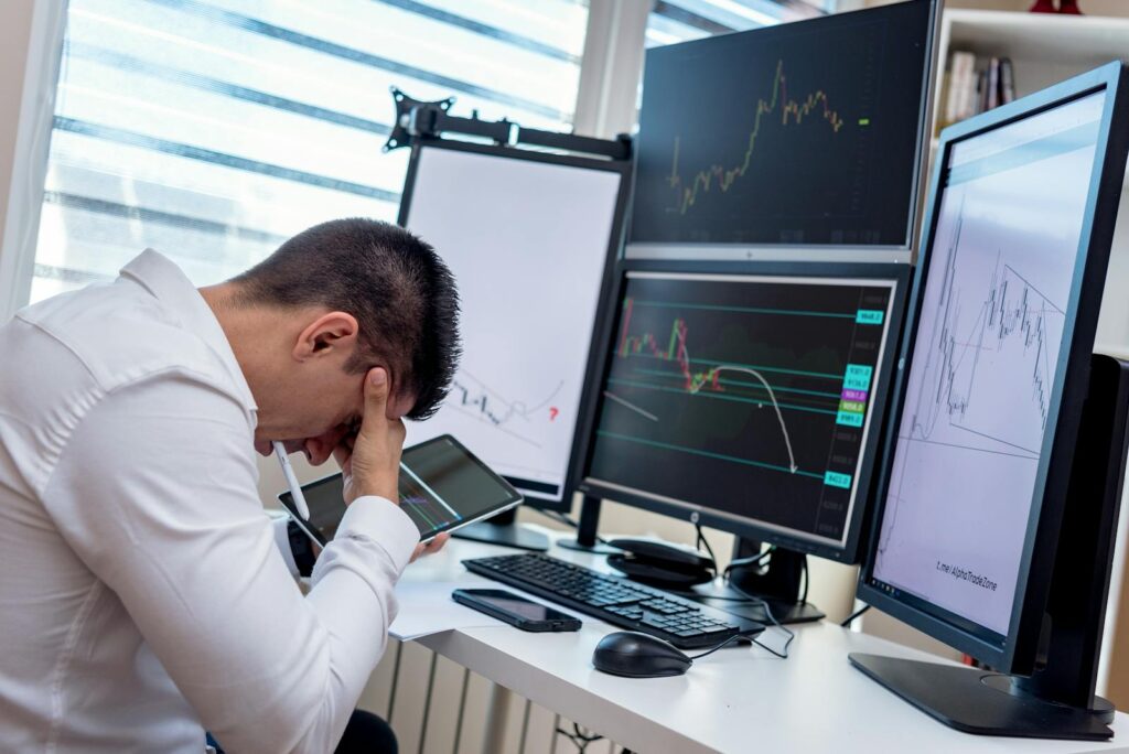 The New Silent Revolution: Why AI Is Making Us Richer — and Yet More Uneasy A stressed trader in an office setting analyzes market data on multiple monitors using a tablet.