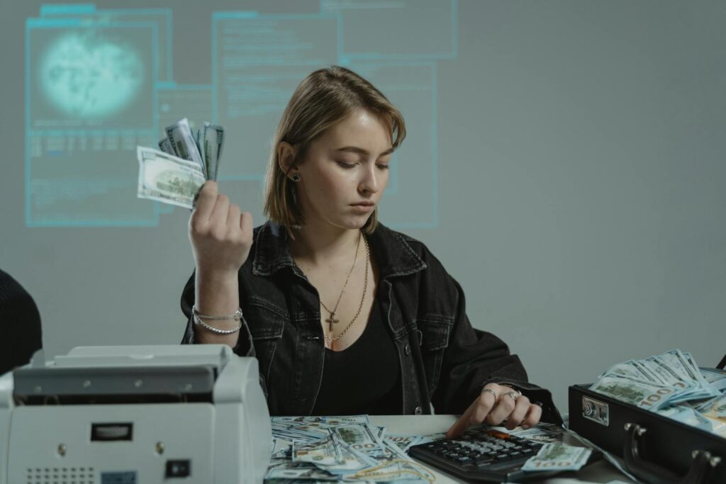 Young woman counting cash using a calculator in an office setting, surrounded by money.