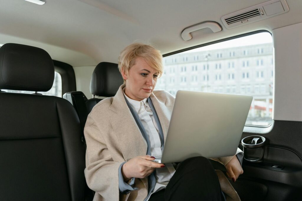 Professional woman working on a laptop inside a car, showcasing productivity on the move.