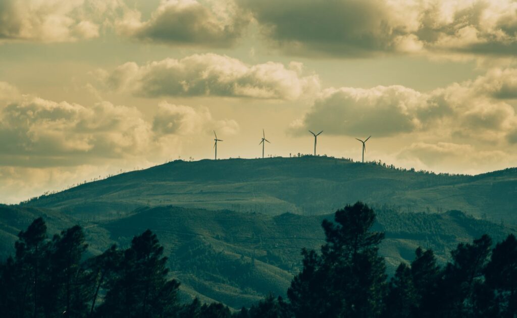 Wind turbines on a hill under a dramatic cloudy sky, showcasing renewable energy amidst nature.