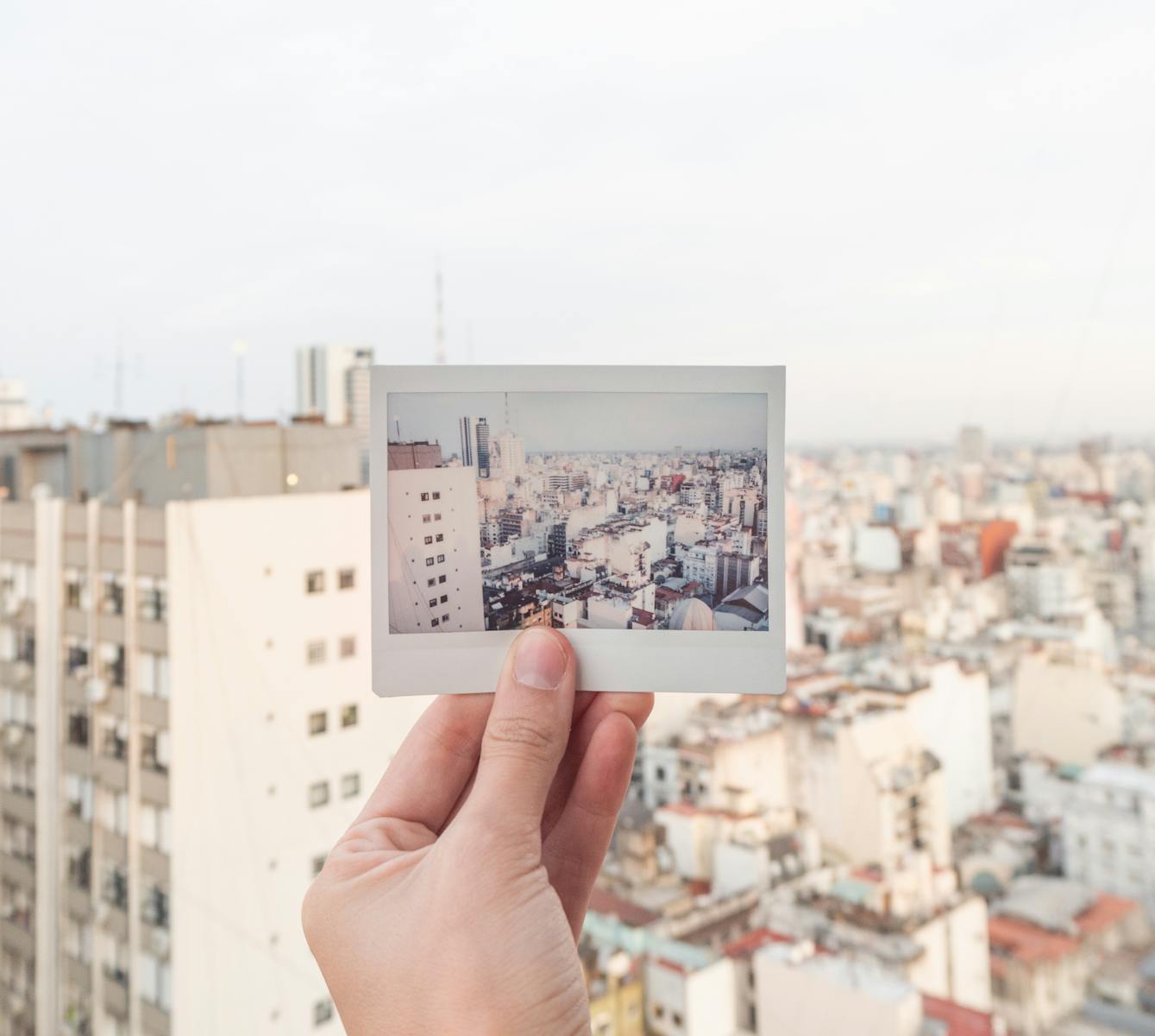 A hand holds a Polaroid of a city skyline against a blurred urban backdrop.