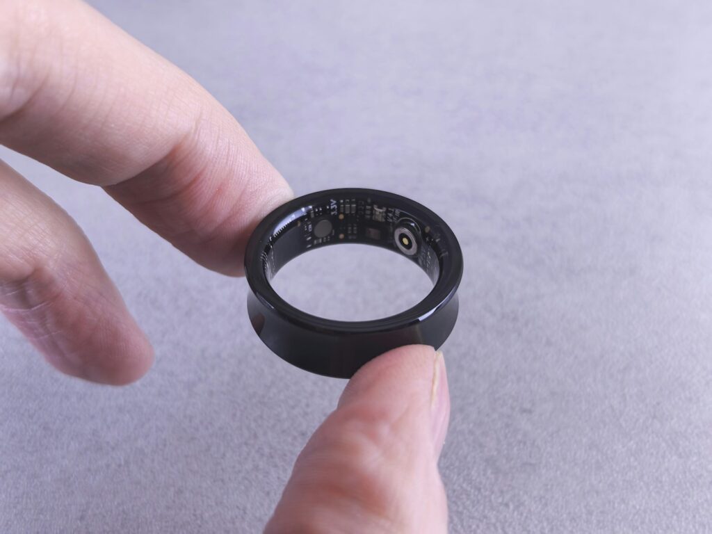 Fingers hold a black smart ring with circuits visible.