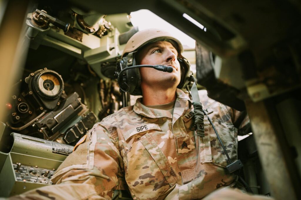 A soldier in camouflage uniform inside an armored vehicle, looking focused.