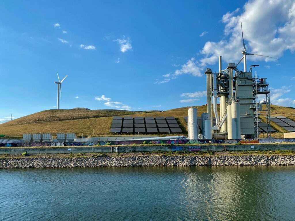 Renewable energy facility in Karlsruhe featuring wind turbines and solar panels beside a river.