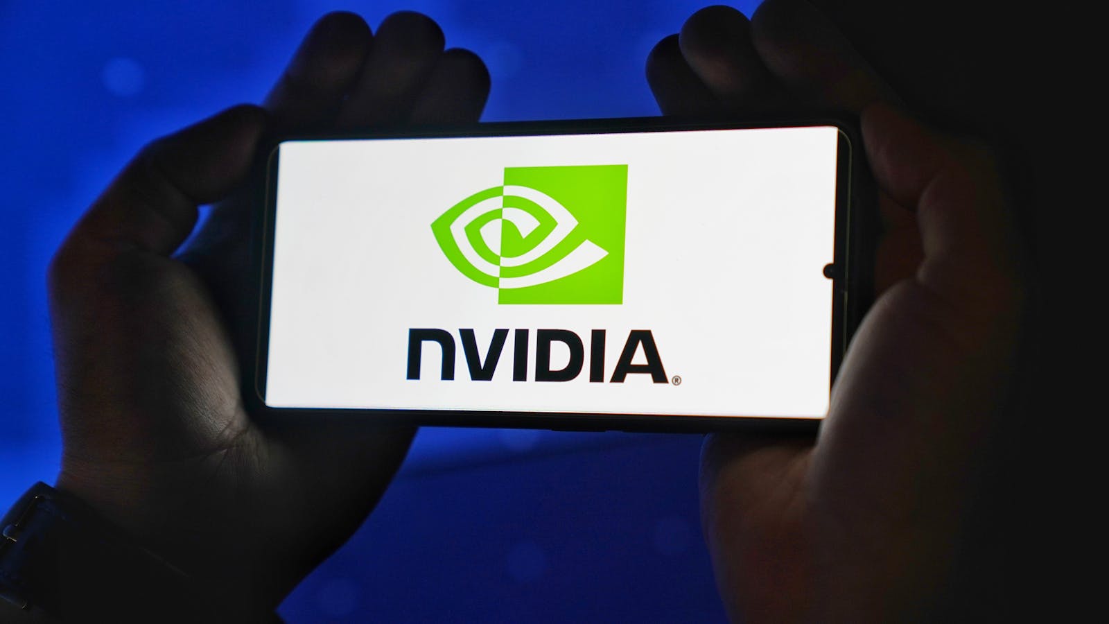 China Says “No Thanks” to America’s New AI Chips Hands holding a smartphone showing the NVIDIA logo on a bright screen.