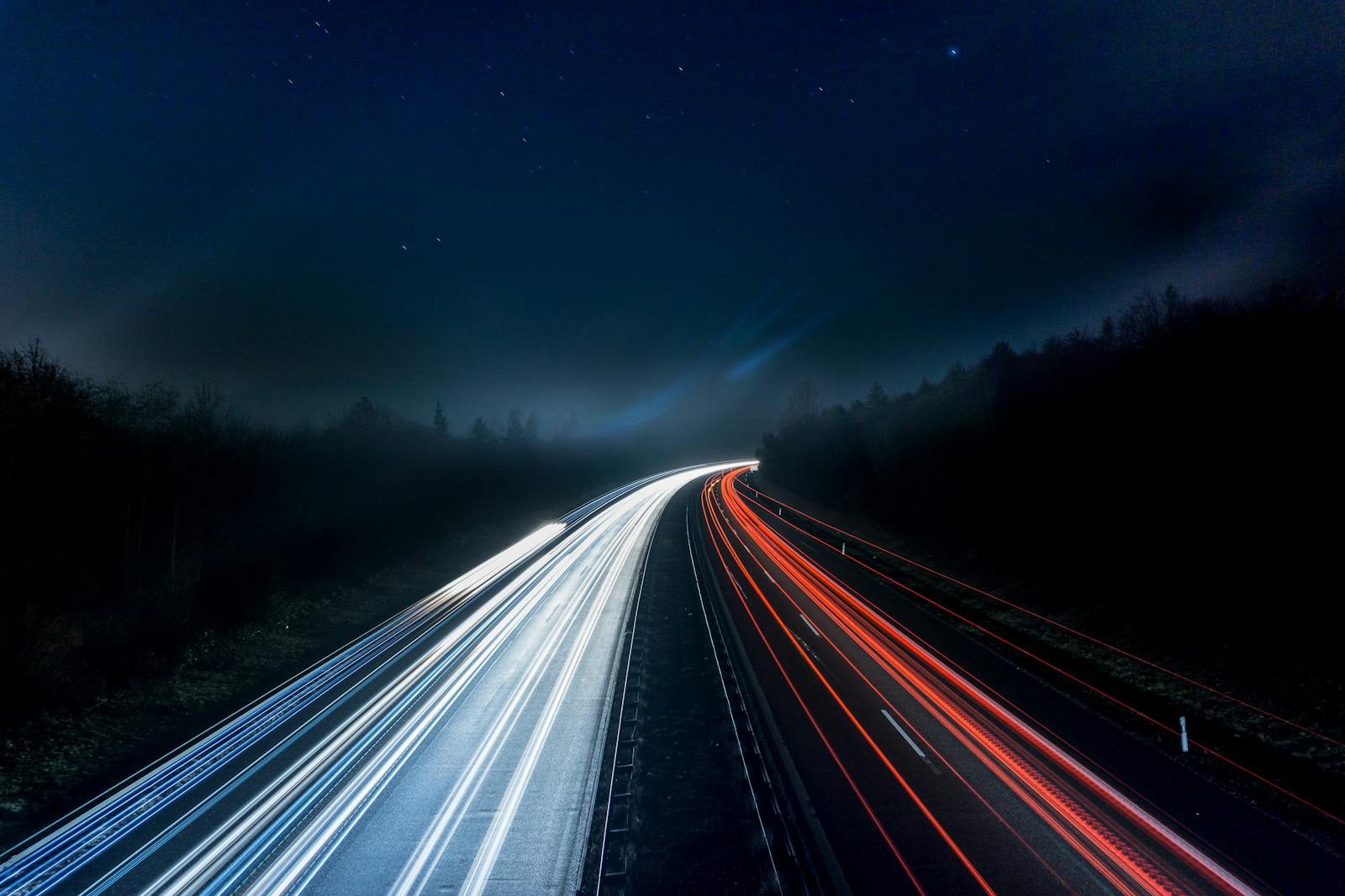 America’s New AI Paradox on Tech Race While Risking Future Long exposure night shot capturing stunning red and white light trails on a highway under a starry sky.