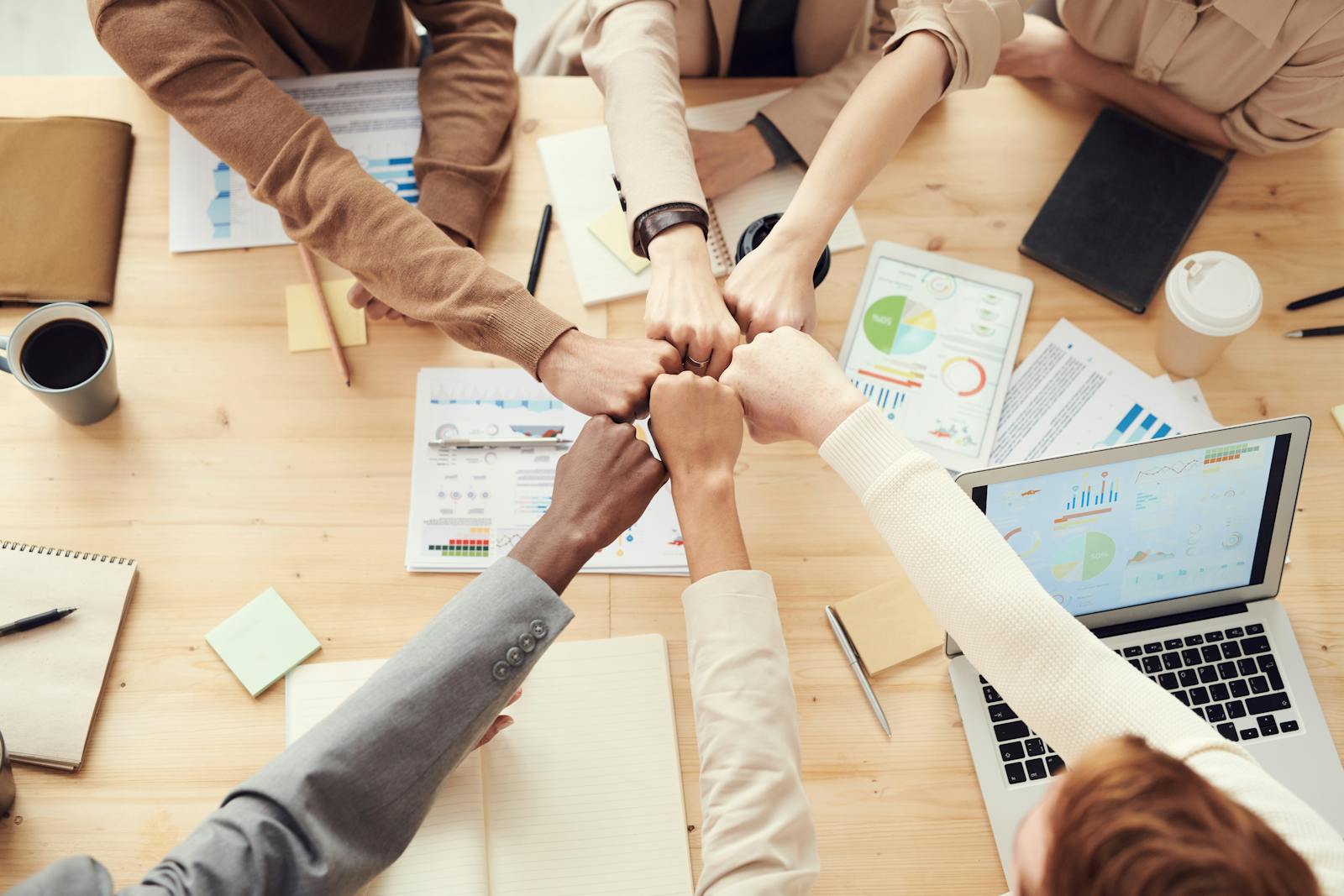Why Strategic Autonomy in AI Is Now a National Priority Top view of a diverse team fist bumping over a meeting table with paperwork and laptops, symbolizing teamwork.