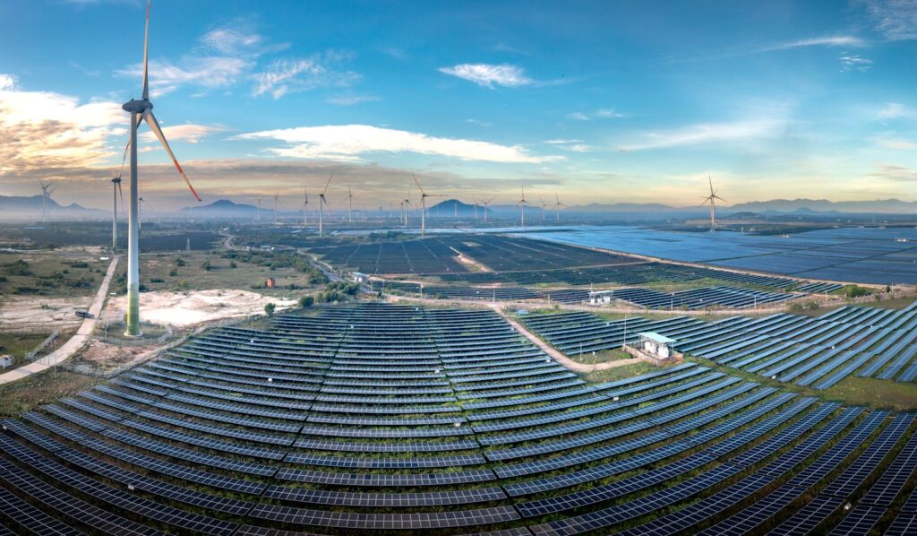 Panoramic aerial view of a renewable energy farm with solar panels and wind turbines in Vietnam at sunset.