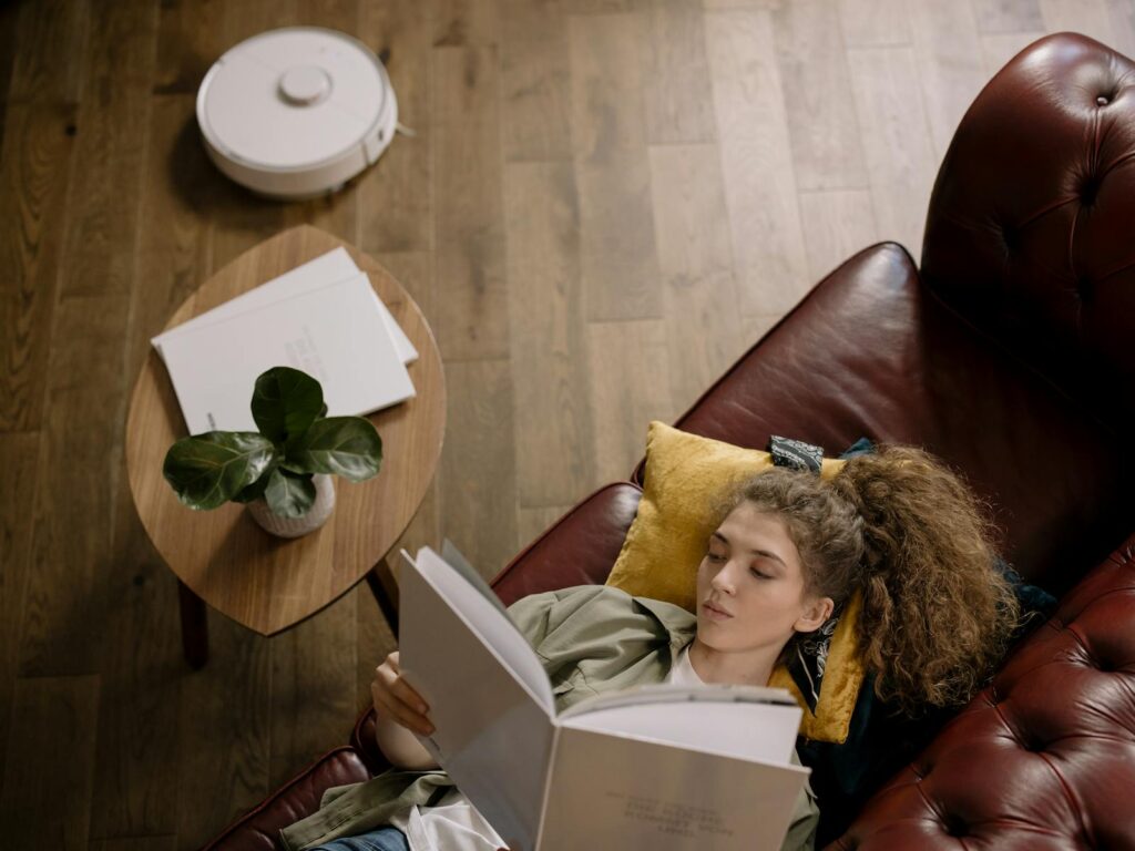 Why Home Robots Still Aren’t Ready for Everyday New Life A woman lying on a couch reading a book, surrounded by cozy home decor.
