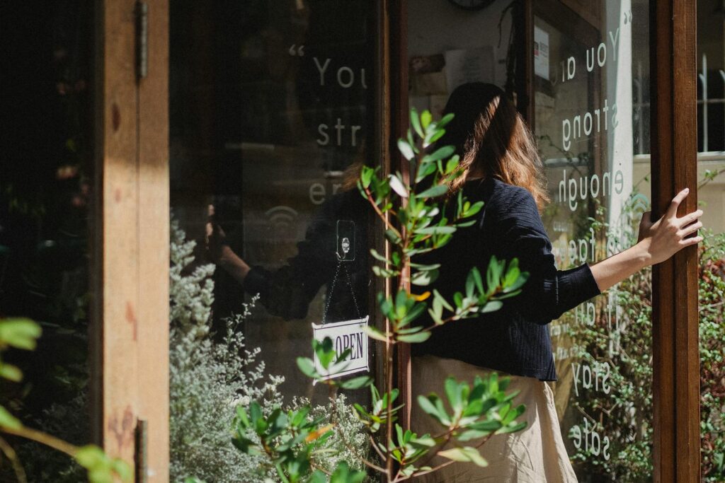 A woman enters a floral shop with glass doors, sunlight streaming in with reflections.