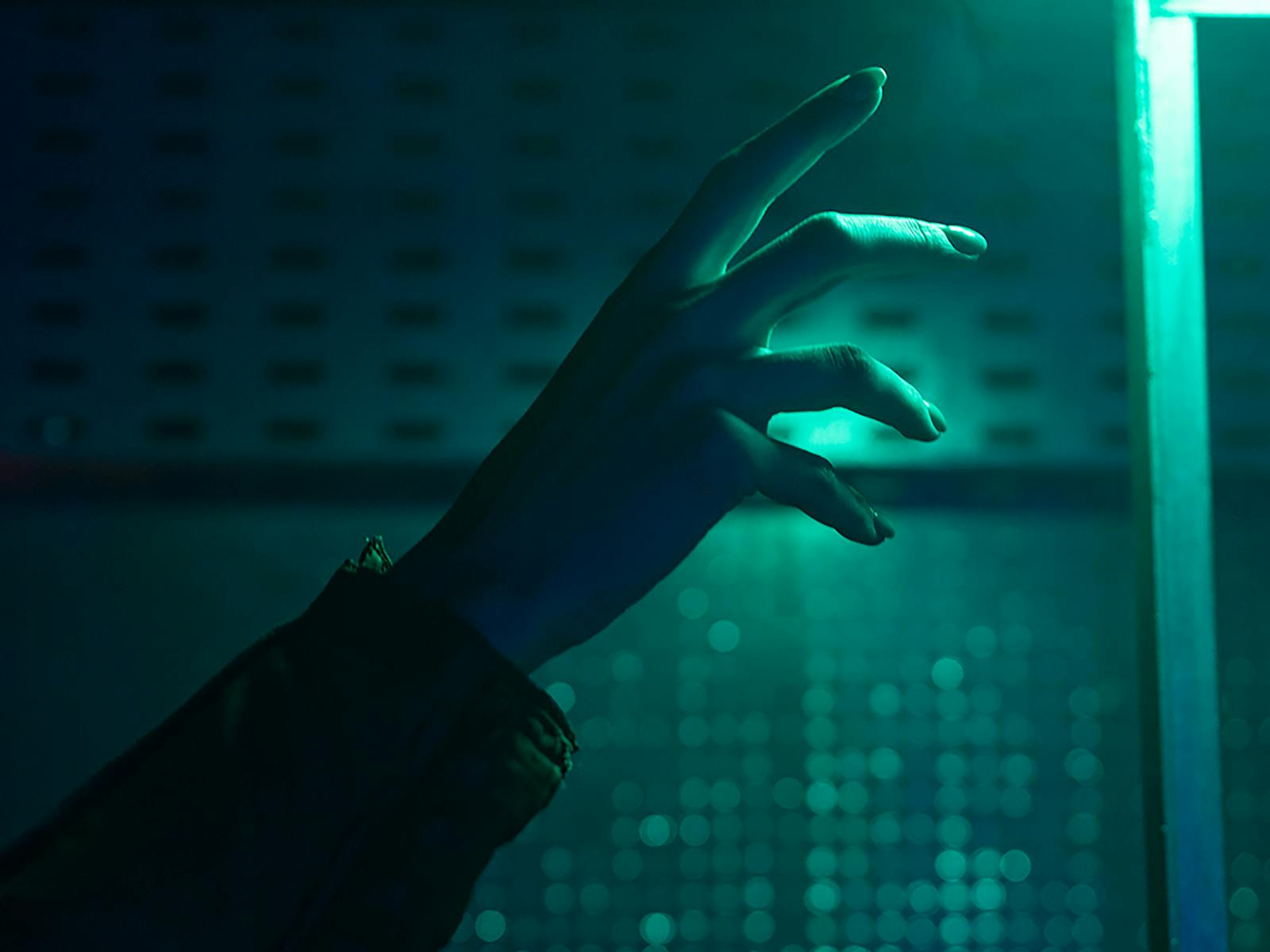 A close-up of a hand reaching out in a dimly lit environment with neon green lighting.