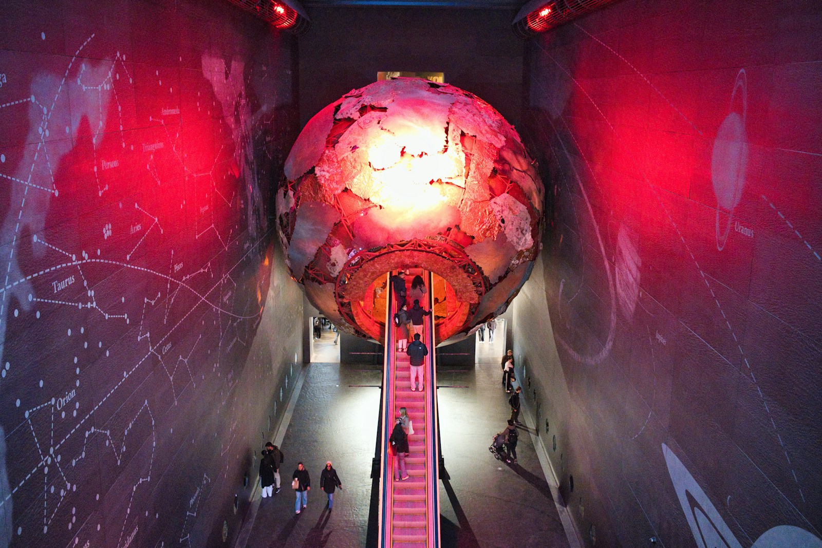People ascend escalator towards large glowing globe