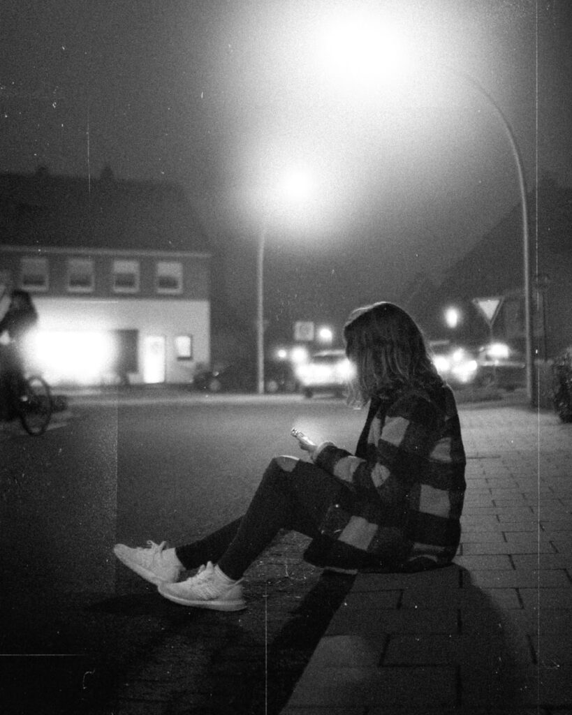 a person sitting on a curb looking at a cell phone