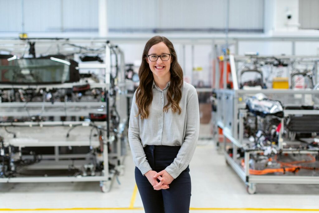 AI Won’t Eliminate Engineering Jobs But What Means New Engineer Smiling woman engineer standing confidently in a modern industrial workshop setting.