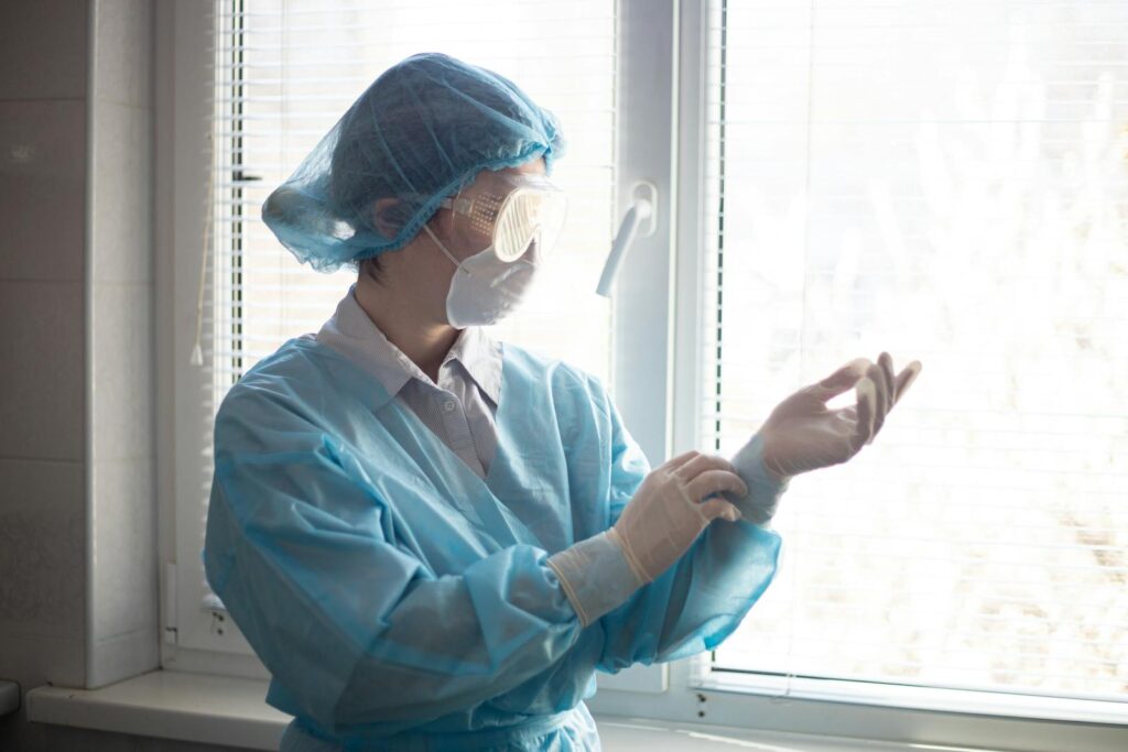 Healthcare worker in protective gear wearing mask and gloves inside a medical facility.