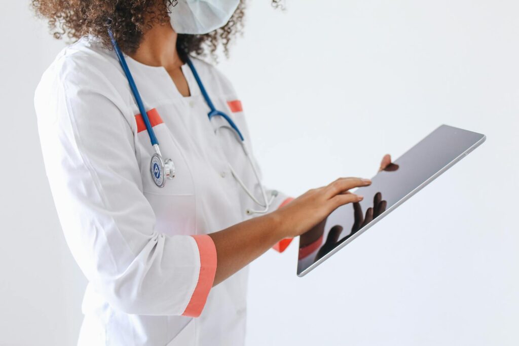 A doctor wearing a face mask and stethoscope using a tablet in a medical setting.