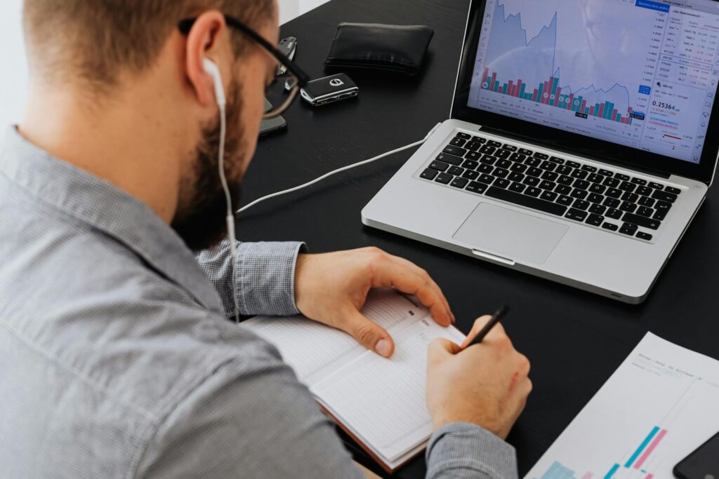 Why the World Gambling Trillions on AI With No Guarantee A businessman analyzing stock data on a laptop while taking notes at a desk.