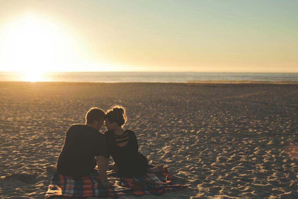 A couple enjoys sunset together on a sandy beach, capturing a moment of love and togetherness.