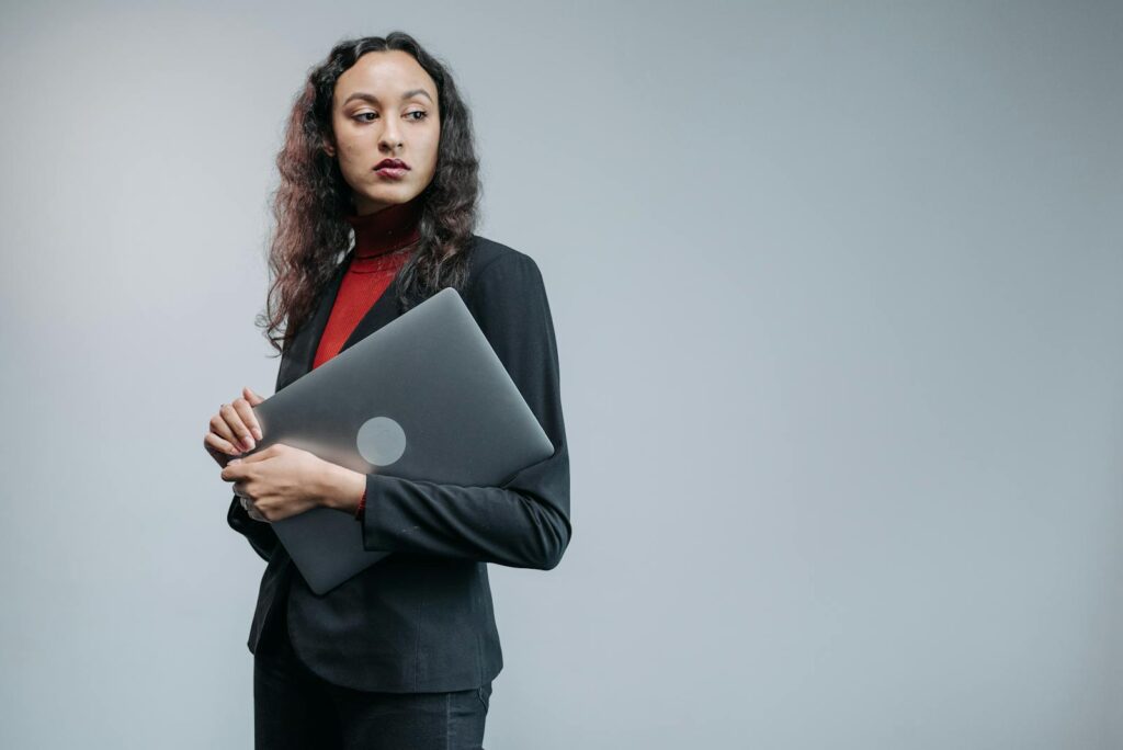 Confident businesswoman in black blazer holding laptop looking over shoulder indoors.