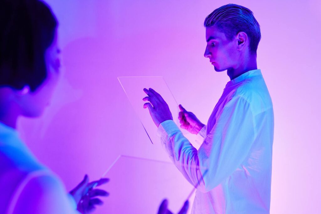 The Technology Trends That Will Define 2026 — Ready or Not Two individuals engaging with futuristic transparent touch screens in a vibrant purple-lit studio.