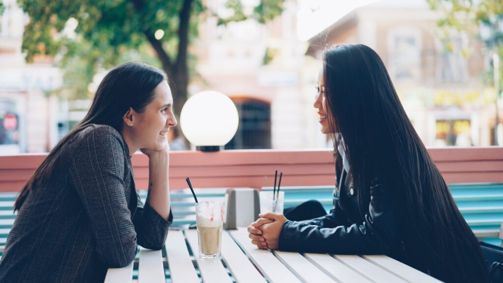 Two women talking at an outdoor cafe table.