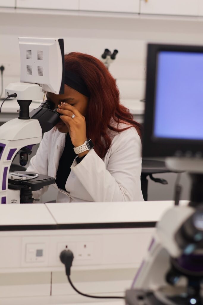 Woman in lab coat looks through microscope