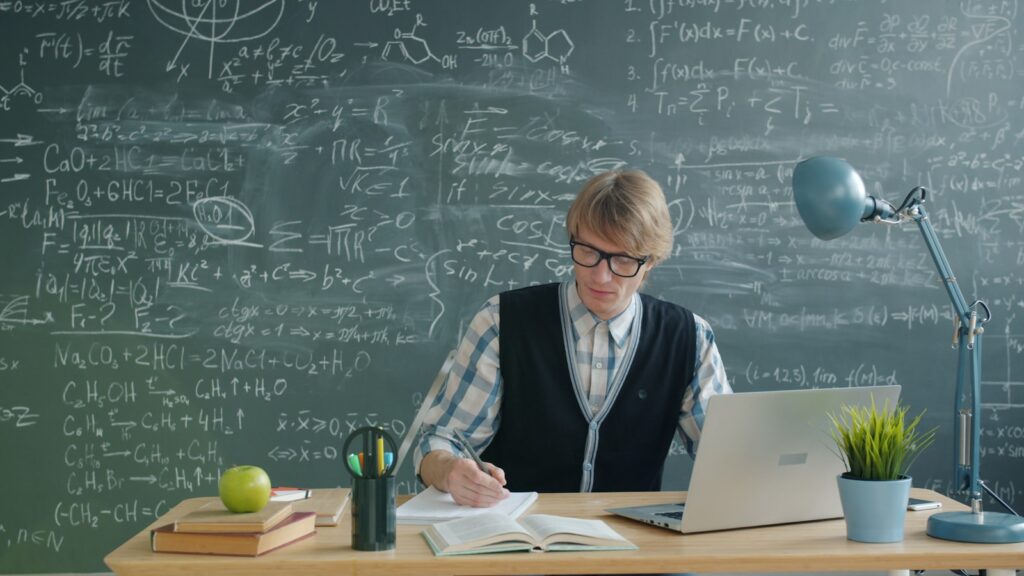 Student studying at a desk with a chalkboard.